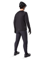 Alpinestars A-Dura Thermal Pant, pantalones de ciclismo de montaña, negro, vista desde una perspectiva trasera con un jersey de manga larga a juego, casco de MTB negro y guantes, equipamiento técnico de ciclismo para clima frío