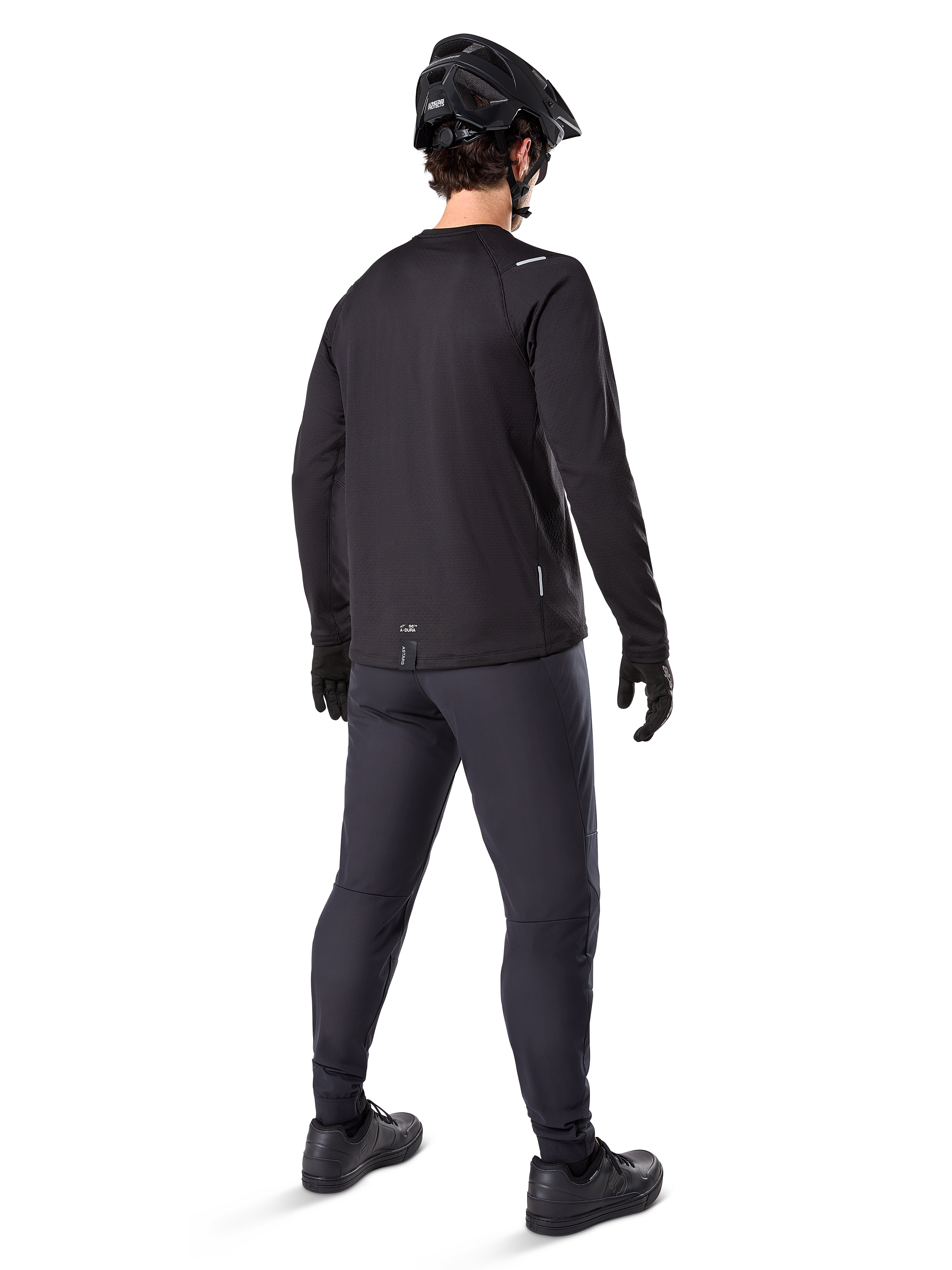 Alpinestars A-Dura Thermal Pant, pantalones de ciclismo de montaña, negro, vista desde una perspectiva trasera con un jersey de manga larga a juego, casco de MTB negro y guantes, equipamiento técnico de ciclismo para clima frío