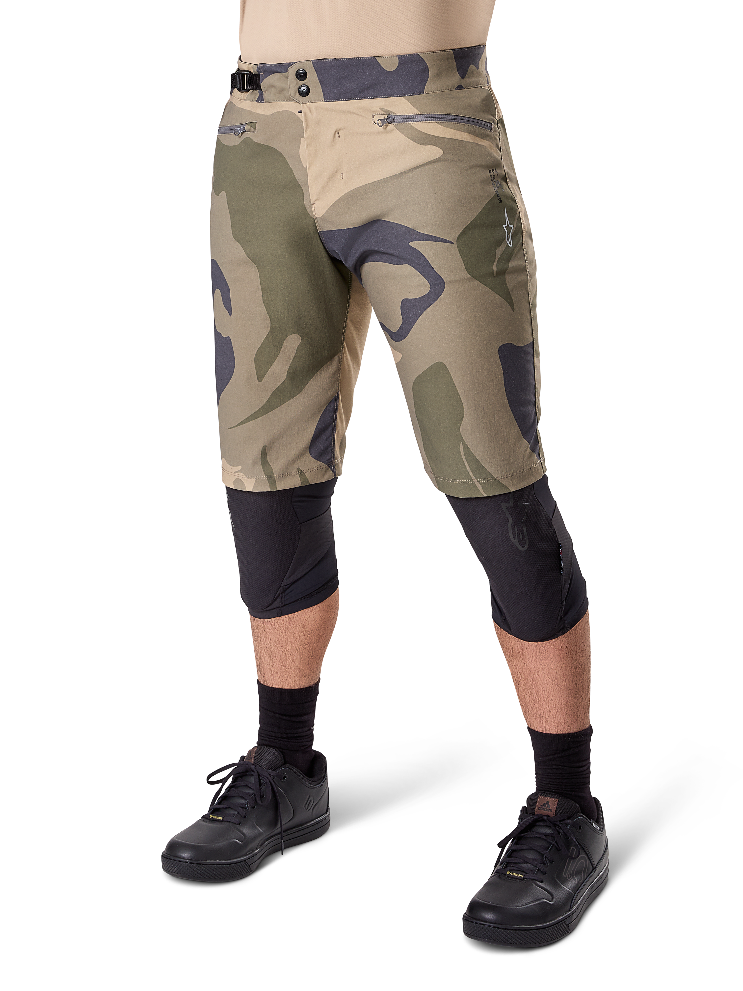 Alpinestars A-Dura Camo Liner Short, shorts de ciclismo de montaña, estampado de camuflaje marrón, vista frontal con bolsillos con cremallera y ajustadores laterales en la cintura, usados con rodilleras negras y zapatillas de ciclismo negras, equipamiento duradero para MTB