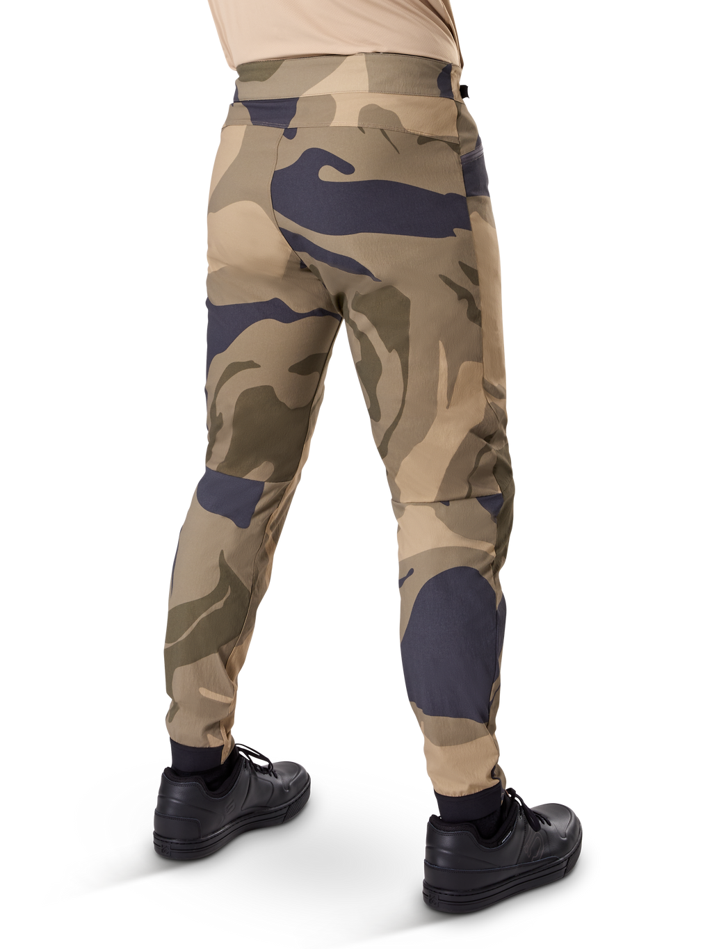 Pantalones Alpinestars A-Dura Camo, pantalones de MTB, estampado de camuflaje marrón con detalles en beige y gris oscuro, vista trasera con zapatillas negras, perneras ajustadas y puños elásticos, tejido elástico en 2 direcciones duradero para ciclismo de montaña