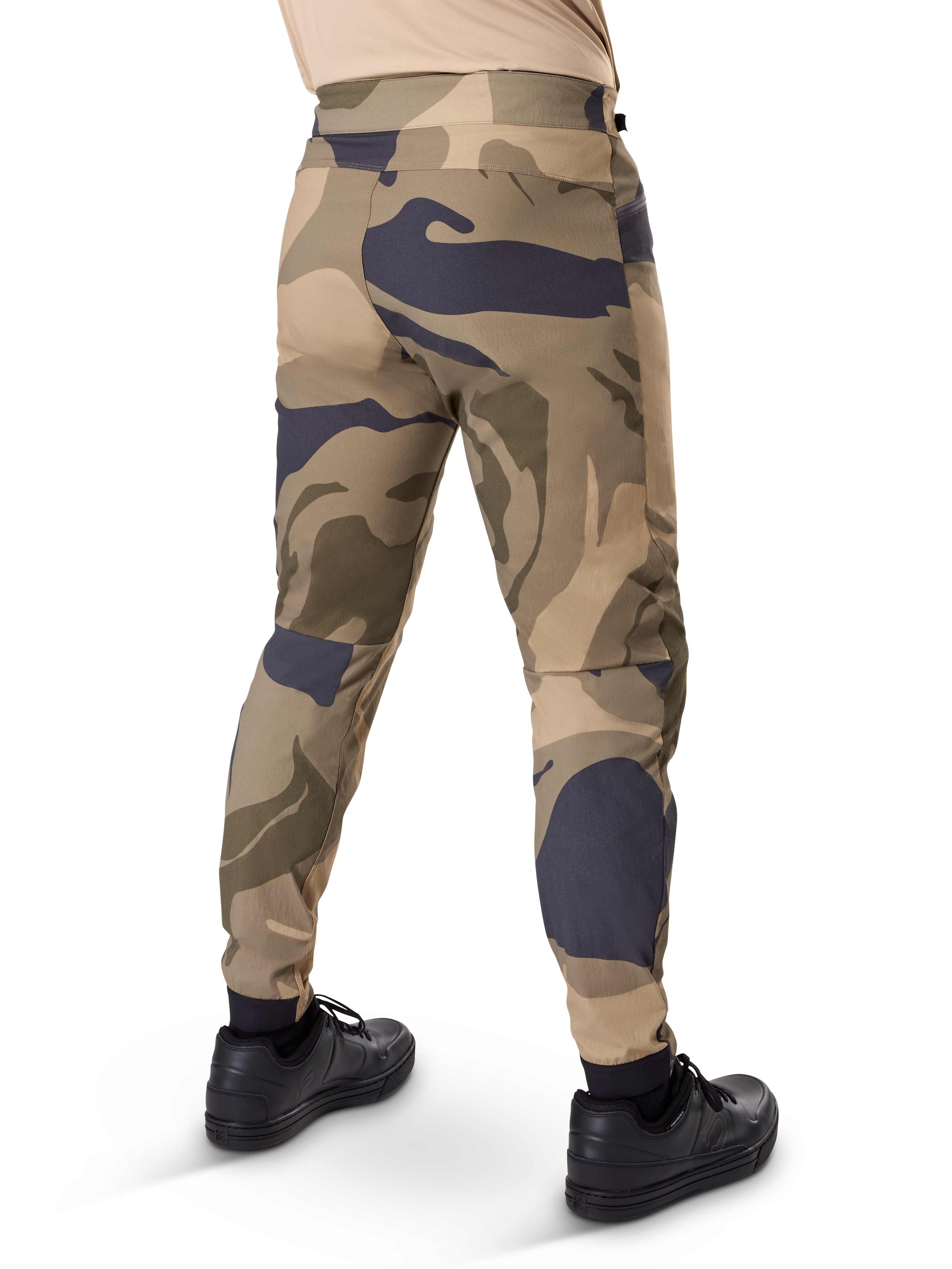 Pantalones Alpinestars A-Dura Camo, pantalones de MTB, estampado de camuflaje marrón con detalles en beige y gris oscuro, vista trasera con zapatillas negras, perneras ajustadas y puños elásticos, tejido elástico en 2 direcciones duradero para ciclismo de montaña