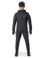 Alpinestars A-Dura Waterproof Pants, pantalones negros de MTB, parte de un conjunto completo de equipamiento de ciclismo de montaña totalmente negro con chaqueta técnica impermeable, casco negro, gafas de sol y guantes, diseñado para la conducción todoterreno en condiciones de clima húmedo.