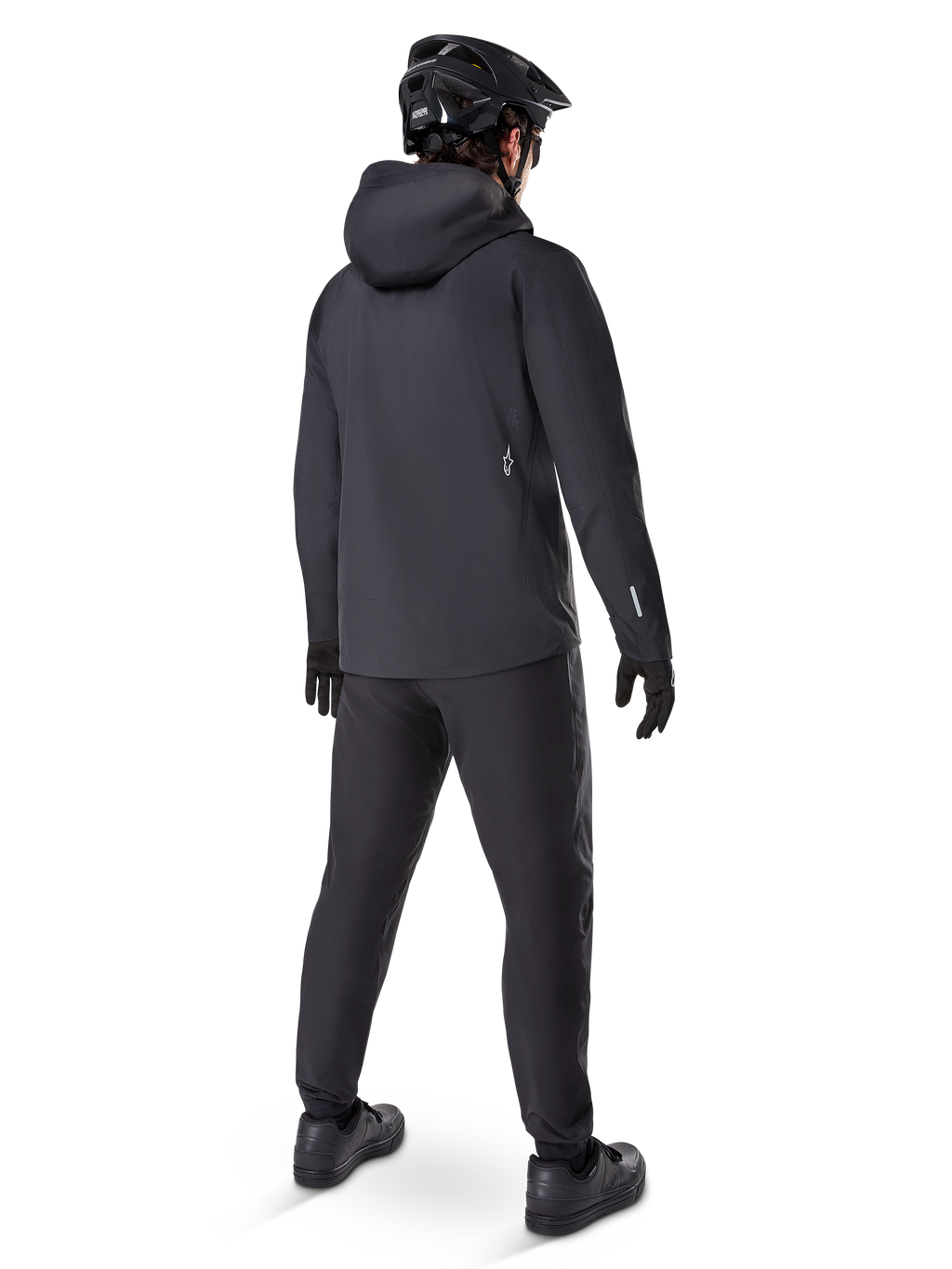 Pantalones Impermeables Alpinestars A-Dura, pantalones de MTB, negro, vistos desde atrás en un ciclista con un conjunto completo de ciclismo de montaña negro que incluye chaqueta con capucha y casco, equipamiento impermeable duradero para senderos embarrados