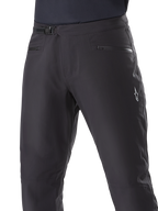 Pantalones Impermeables Alpinestars A-Dura, pantalones de ciclismo de montaña, negros, primer plano de la cintura que muestra el sistema de cierre de trinquete y los bolsillos con cremallera, con el logotipo blanco de Alpinestars en el muslo, tejido duradero para rutas con clima húmedo