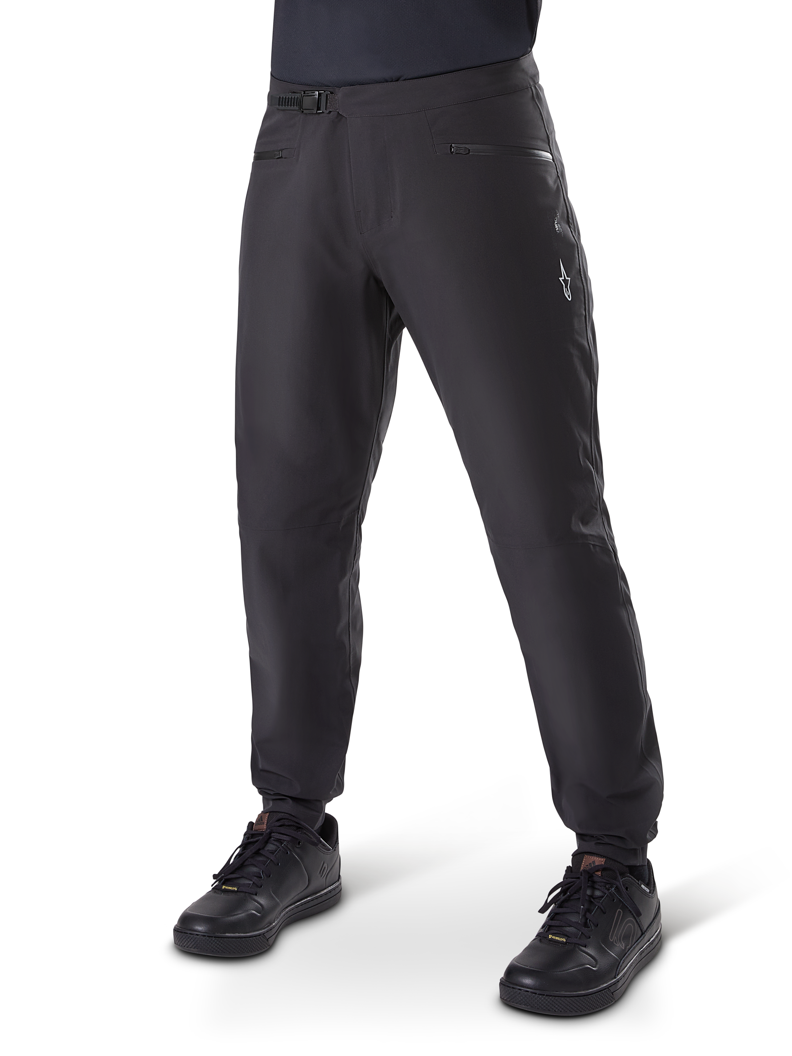 Pantalones impermeables Alpinestars A-Dura, pantalones de ciclismo MTB, color negro, con cierre de trinquete en la cintura, bolsillos con cremallera y logotipo Astars blanco en el muslo, mostrados con zapatillas de ciclismo negras para rutas por senderos en cualquier clima