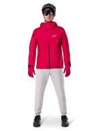 Alpinestars A-Dura Waterproof Pants, pantalones de MTB en color gris titanio, combinados con una chaqueta roja con capucha, guantes rojos y un casco negro de ciclismo de montaña, equipamiento ciclista impermeable profesional para condiciones de senderos húmedos