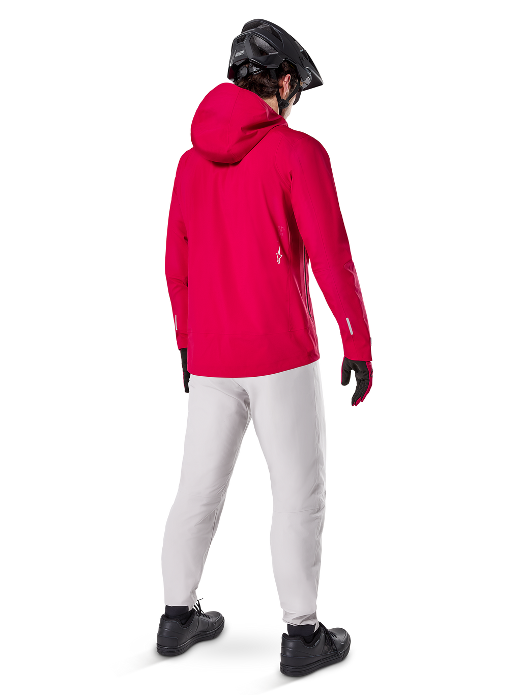 Alpinestars A-Dura Waterproof Pants en color Titanium, vista trasera de un ciclista con los pantalones técnicos para bicicleta de montaña en gris claro, chaqueta roja con capucha y casco negro, equipamiento impermeable y duradero para ciclismo en condiciones húmedas