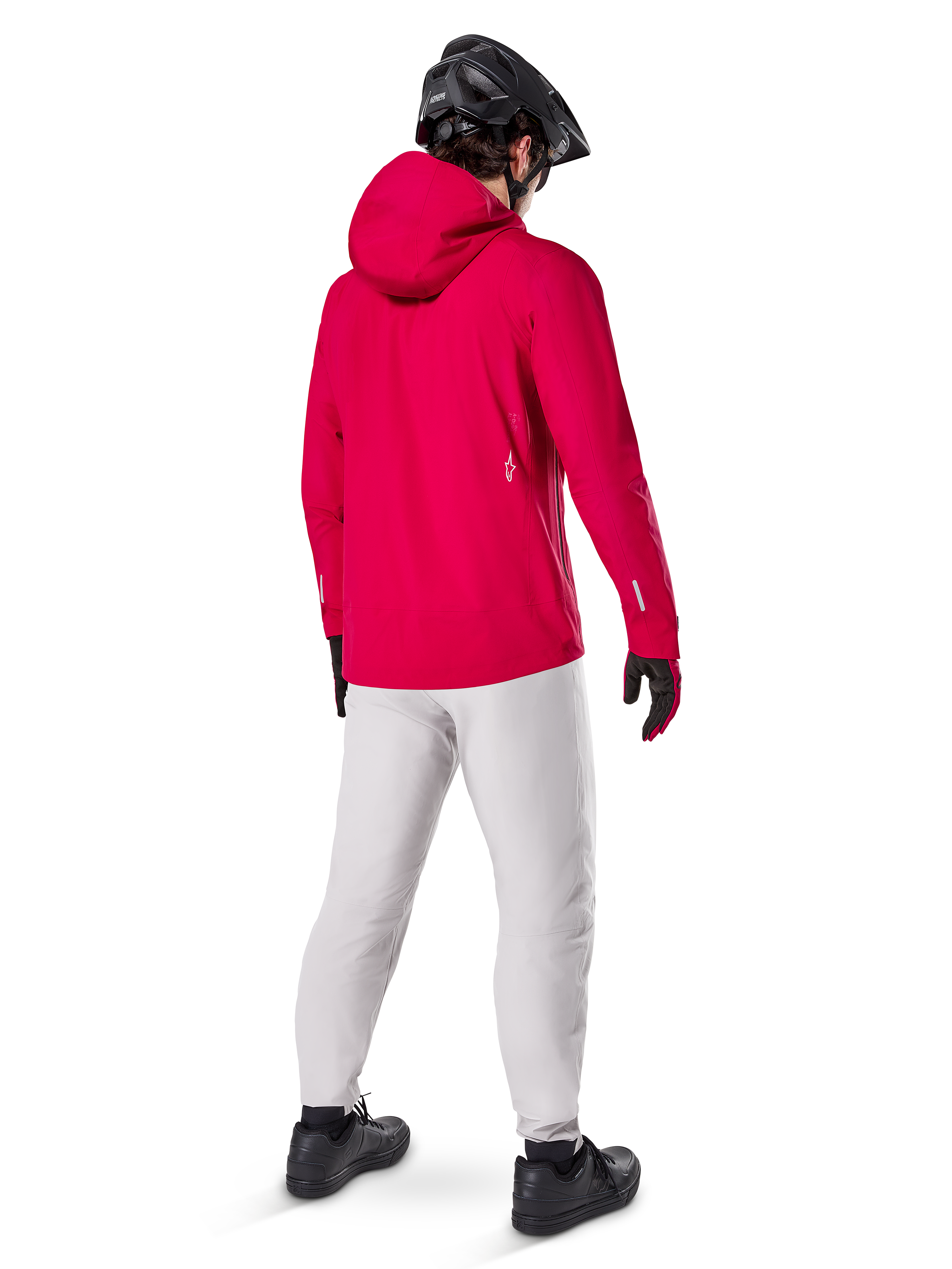 Alpinestars A-Dura Waterproof Pants en color Titanium, vista trasera de un ciclista con los pantalones técnicos para bicicleta de montaña en gris claro, chaqueta roja con capucha y casco negro, equipamiento impermeable y duradero para ciclismo en condiciones húmedas