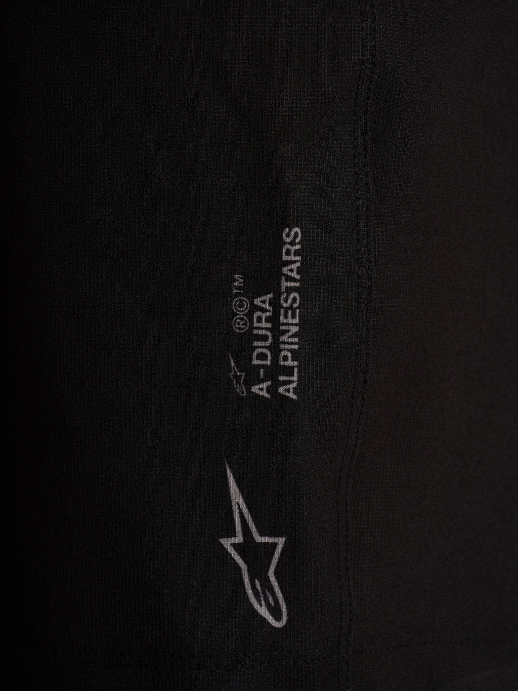 Detalle del logotipo Alpinestars en pantalones cortos A-Dura Ride Liner negros de tejido elástico.