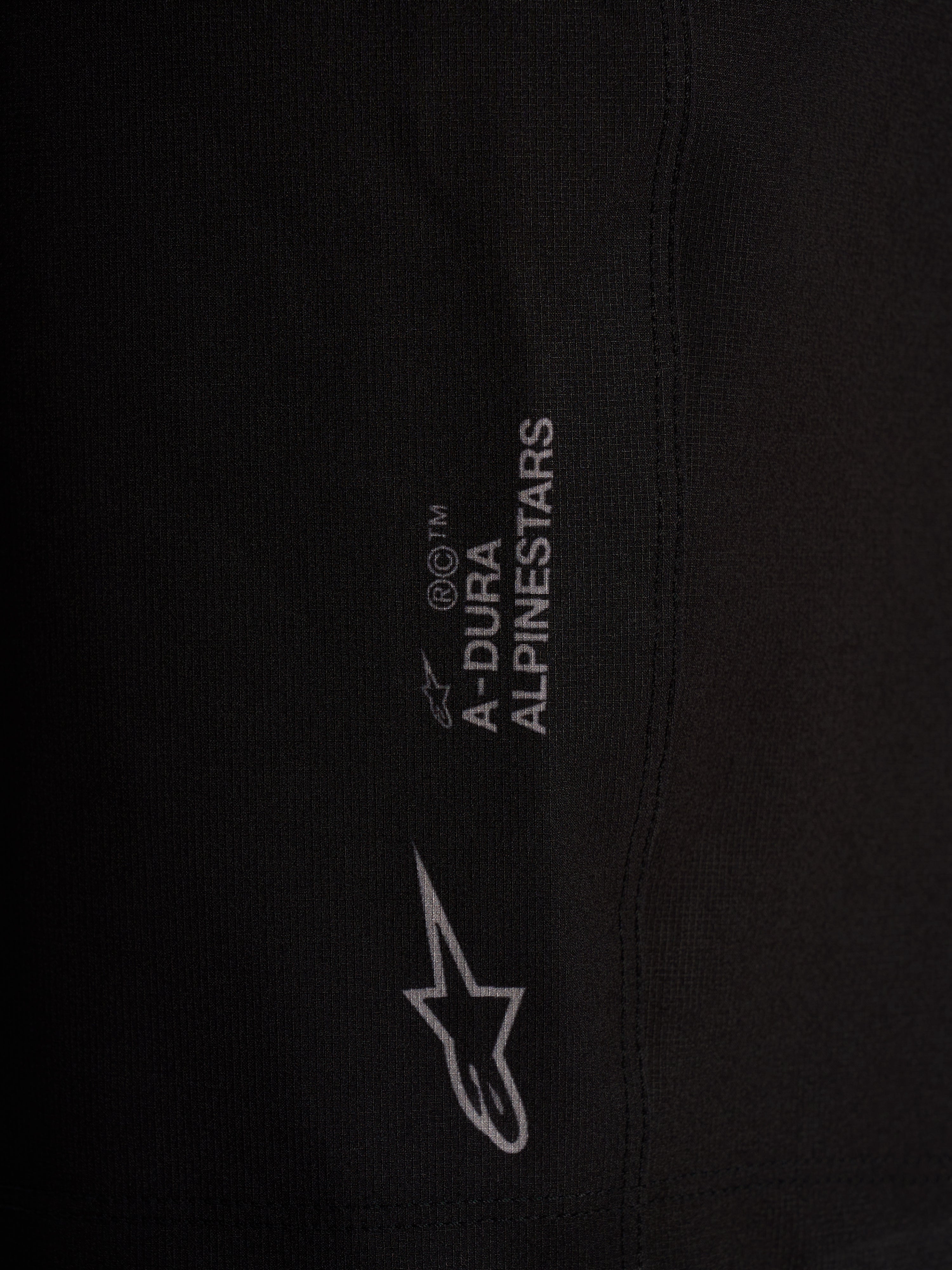 Detalle del logotipo Alpinestars en pantalones cortos A-Dura Ride Liner negros de tejido elástico.