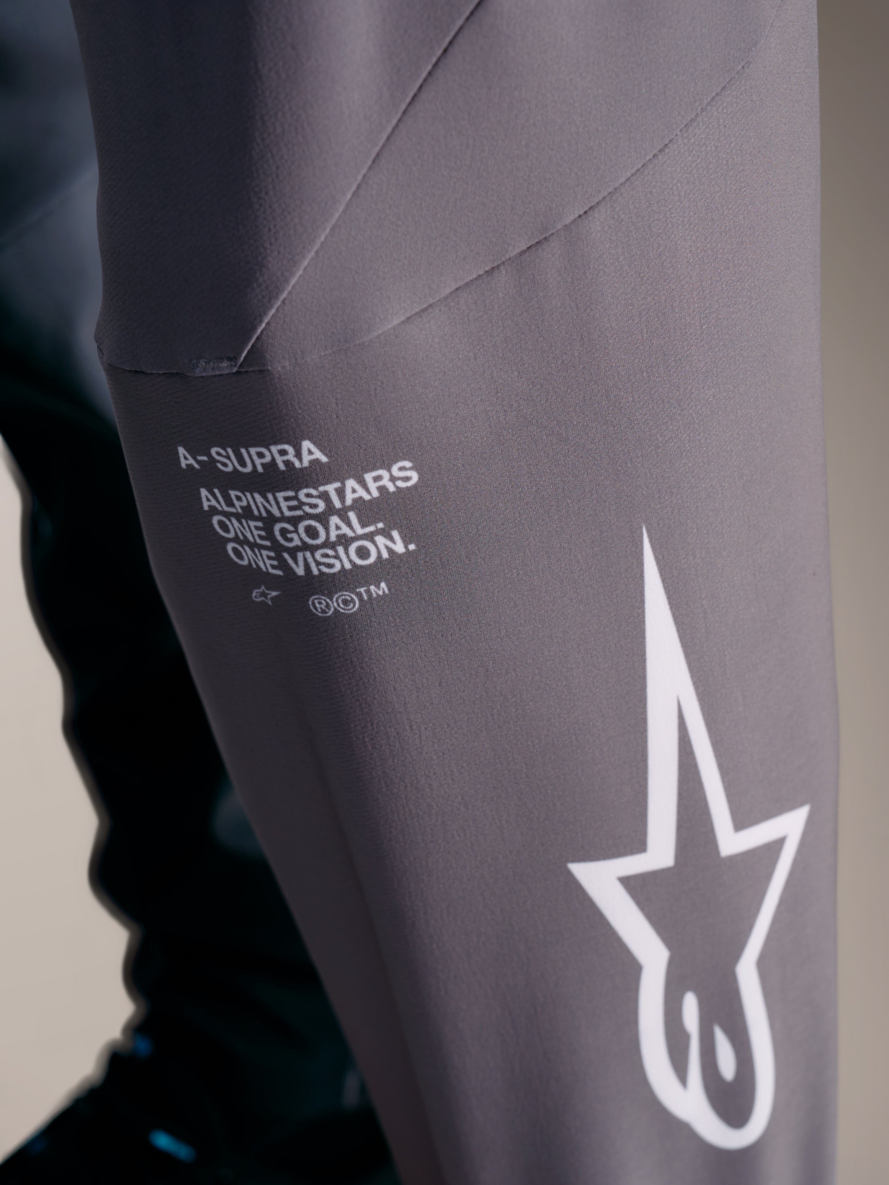 Pantalones A-Supra Elite grises con branding blanco de Alpinestars y lema 'One Goal. One Vision.', diseño de competición.