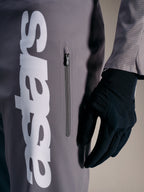 Pantalones A-Supra Elite Faded Gray con logo blanco y bolsillo vertical con cremallera, diseñados para el rendimiento en MTB.