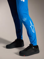 Pantalones A-Supra Elite en azul brillante con logotipo Astars blanco en la pierna y zapatillas de MTB negras.