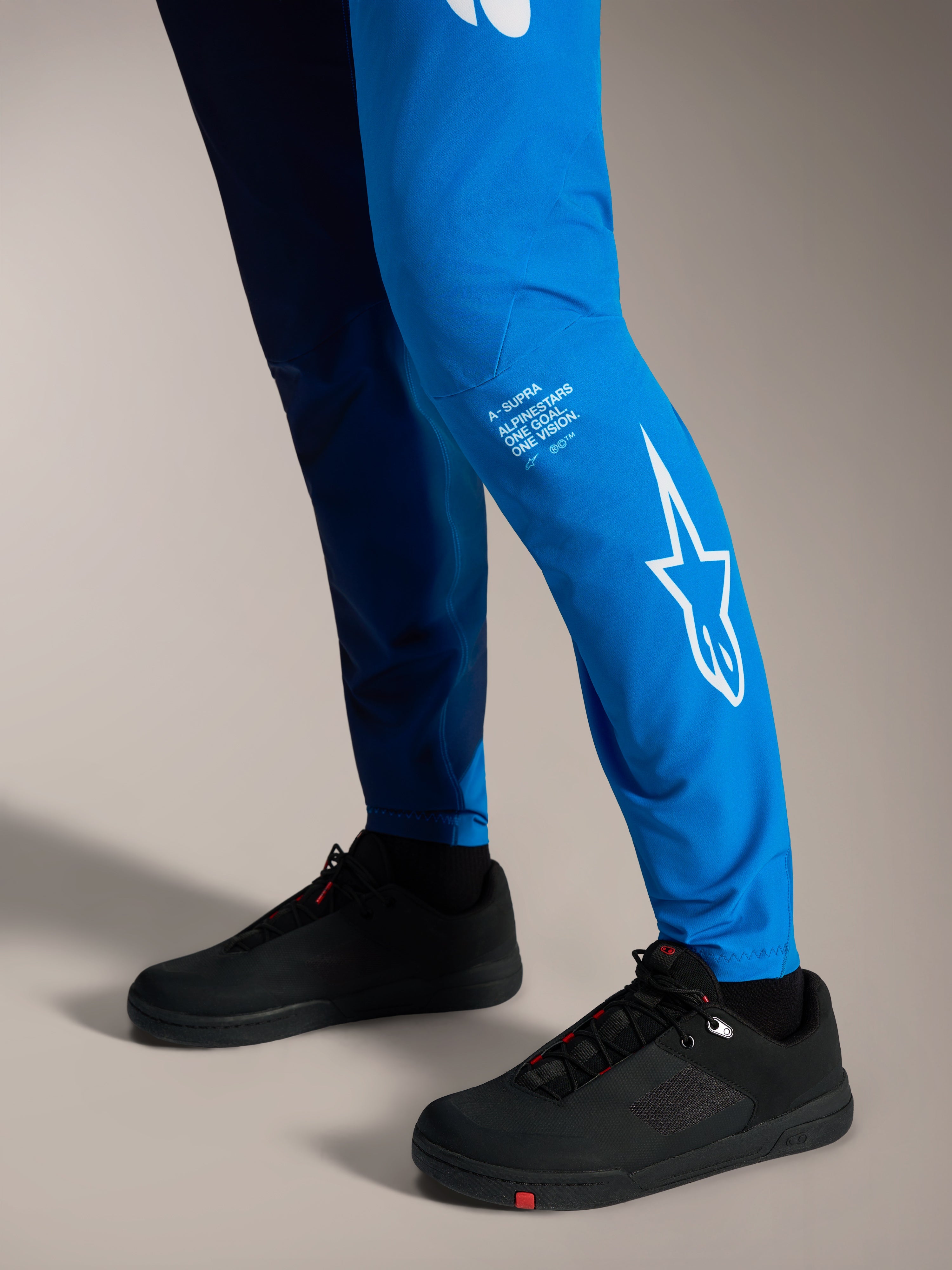 Pantalones A-Supra Elite en azul brillante con logotipo Astars blanco en la pierna y zapatillas de MTB negras.