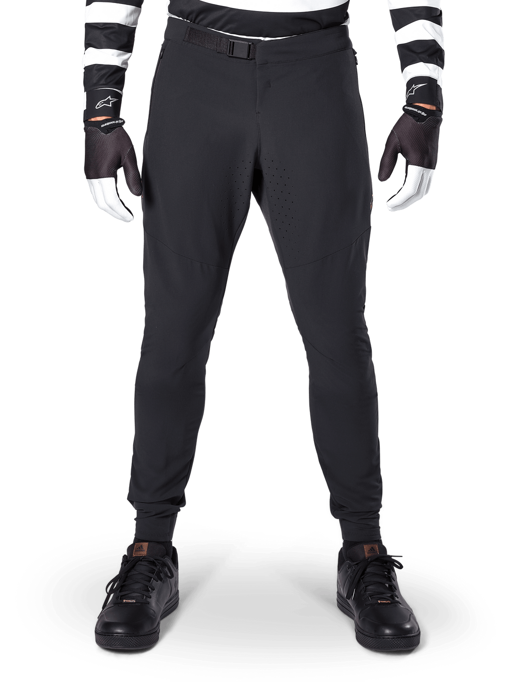 Alpinestars A-Aria Elite Pants, pantalones de MTB en color negro, vista frontal que muestra las perforaciones láser y el cierre de hebilla magnética, usados con jersey de rayas blancas y negras y guantes negros, equipamiento de ciclismo de alto rendimiento para senderos