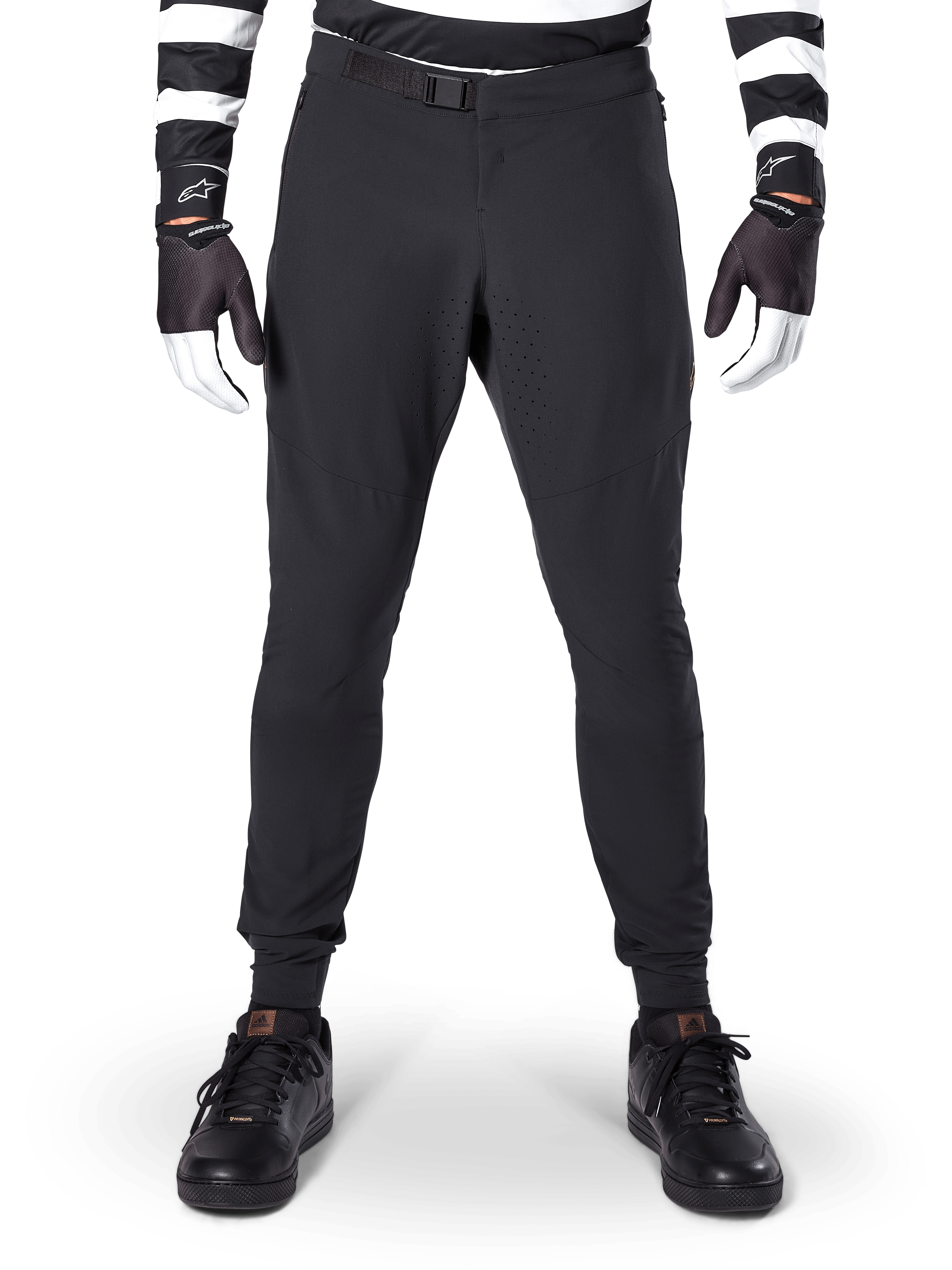 Alpinestars A-Aria Elite Pants, pantalones de MTB en color negro, vista frontal que muestra las perforaciones láser y el cierre de hebilla magnética, usados con jersey de rayas blancas y negras y guantes negros, equipamiento de ciclismo de alto rendimiento para senderos