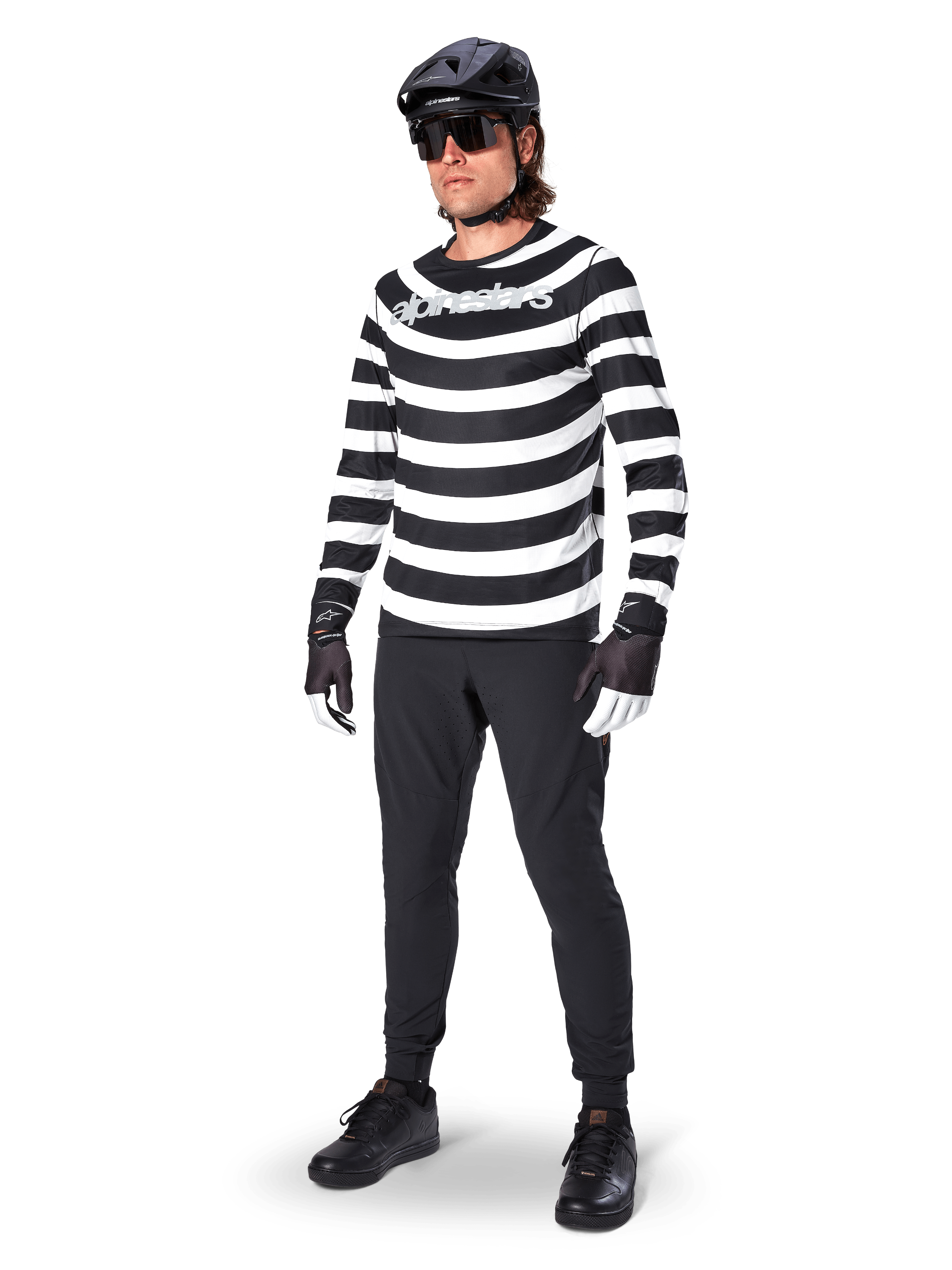Pantalones Alpinestars A-Aria Elite, pantalones de MTB negros, usados por un ciclista con un jersey de manga larga a rayas blancas y negras, casco negro, gafas de sol y guantes blancos y negros, equipamiento de alto rendimiento para ciclismo todoterreno
