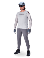 Pantalones Alpinestars A-Aria Elite, pantalones de MTB gris oscuro, usados por un ciclista con jersey de manga larga gris claro y casco gris, con perforaciones láser para ventilación en los muslos y ajuste de rendimiento cónico para ciclismo de montaña