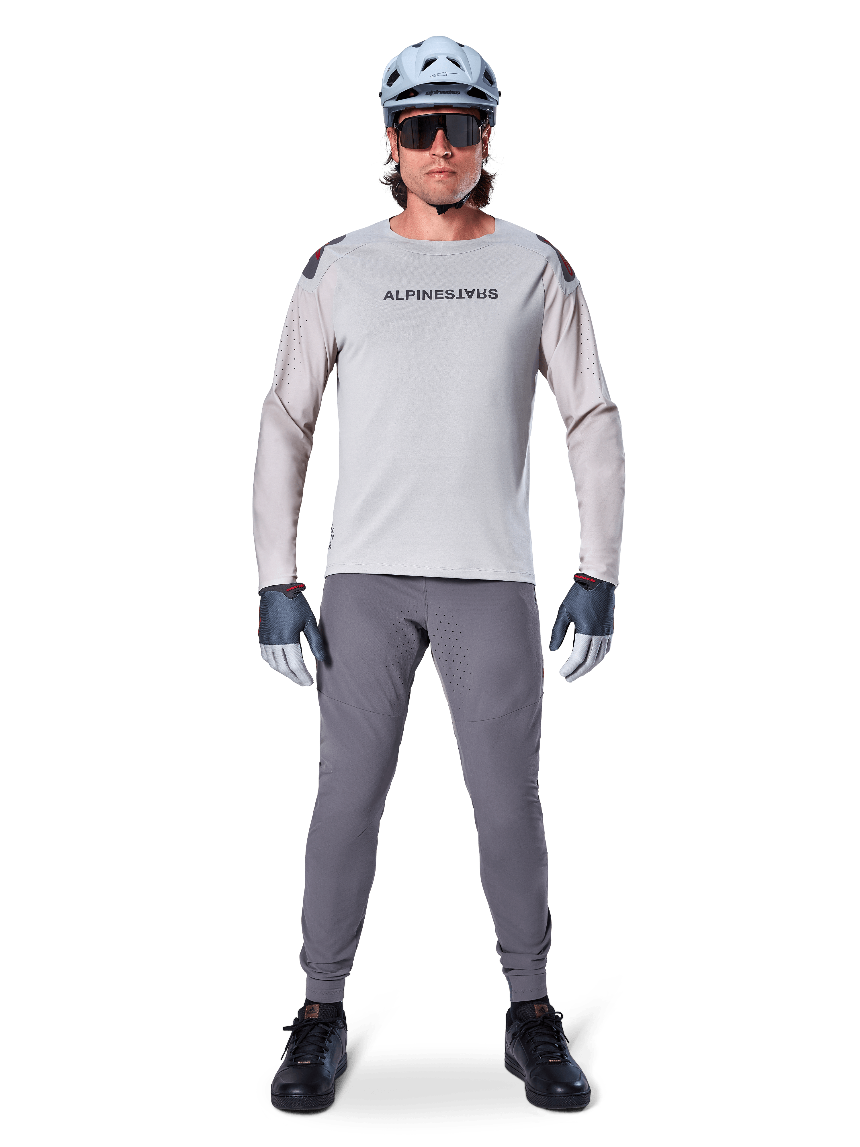 Pantalones Alpinestars A-Aria Elite, pantalones de ciclismo de montaña gris oscuro, usados por un ciclista con jersey de manga larga gris claro, casco azul claro y calzado negro, con perforaciones láser visibles en la parte interna de las piernas y un ajuste de rendimiento entallado