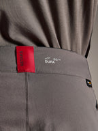 Alpinestars A-Dura Elite Pants, pantalones de MTB, gris oscuro, primer plano de la cintura que muestra una etiqueta ASTARS roja y el logo DURA blanco, con tejido Cordura texturizado y detalles de marca premium