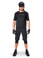 Ciclista de montaña masculino con shorts Alpinestars A-Aria Elite en color negro, combinados con un jersey de manga corta Alpinestars negro a juego, casco, guantes y rodilleras negros, conjunto completo de equipamiento para ciclismo todoterreno
