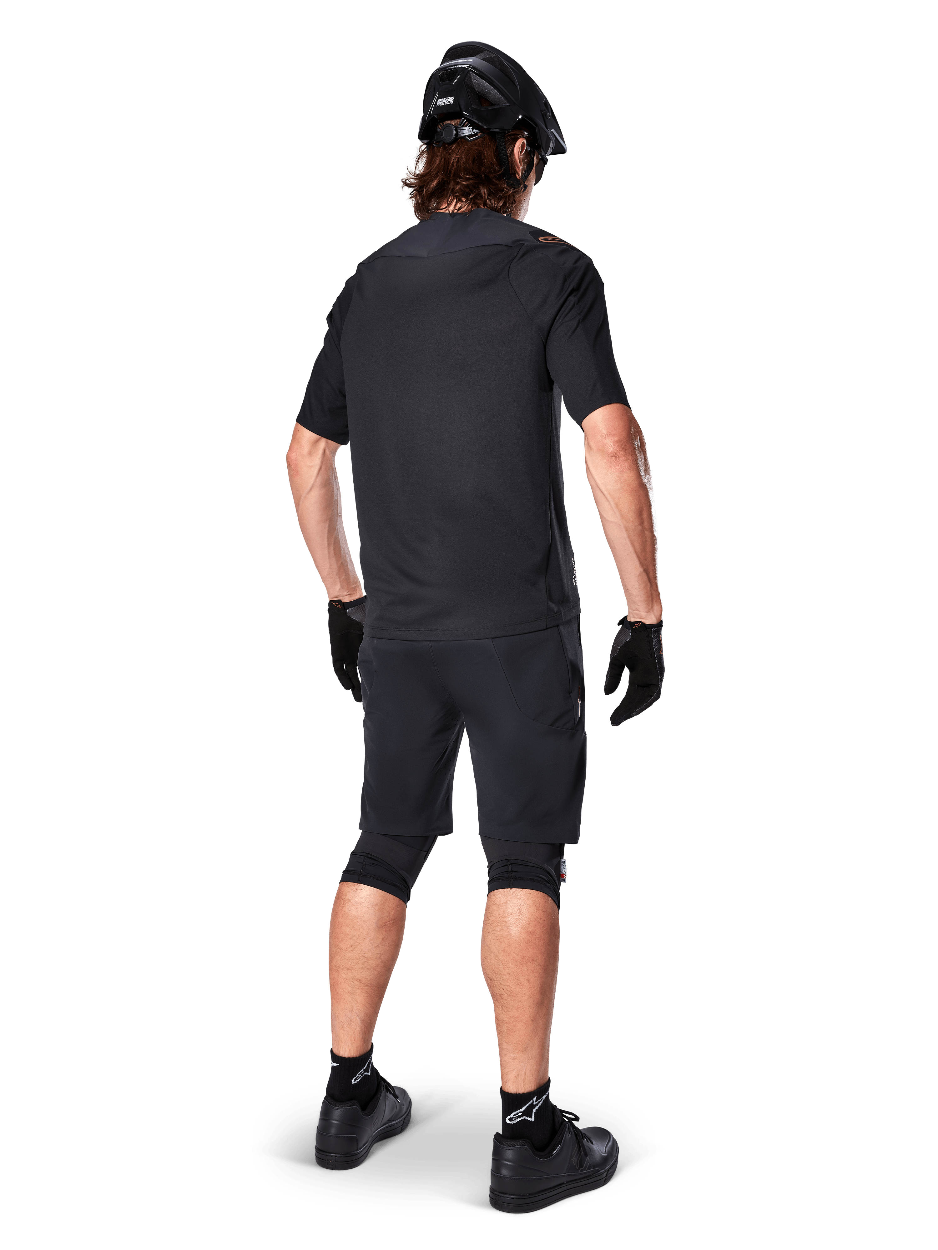 Vista trasera de un ciclista de montaña que viste los shorts Alpinestars A-Aria Elite en negro, combinados con un maillot de manga corta negro a juego, casco negro, guantes y zapatillas de MTB, mostrando un conjunto completo de alto rendimiento para ciclismo de montaña.