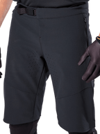 Alpinestars A-Aria Elite Shorts en color negro, vista en primer plano de la zona de la cintura y el muslo, con cierre de hebilla magnética, bolsillos con cremallera y perforaciones de ventilación cortadas con láser, usados con guantes de ciclismo negros para ciclismo de montaña.