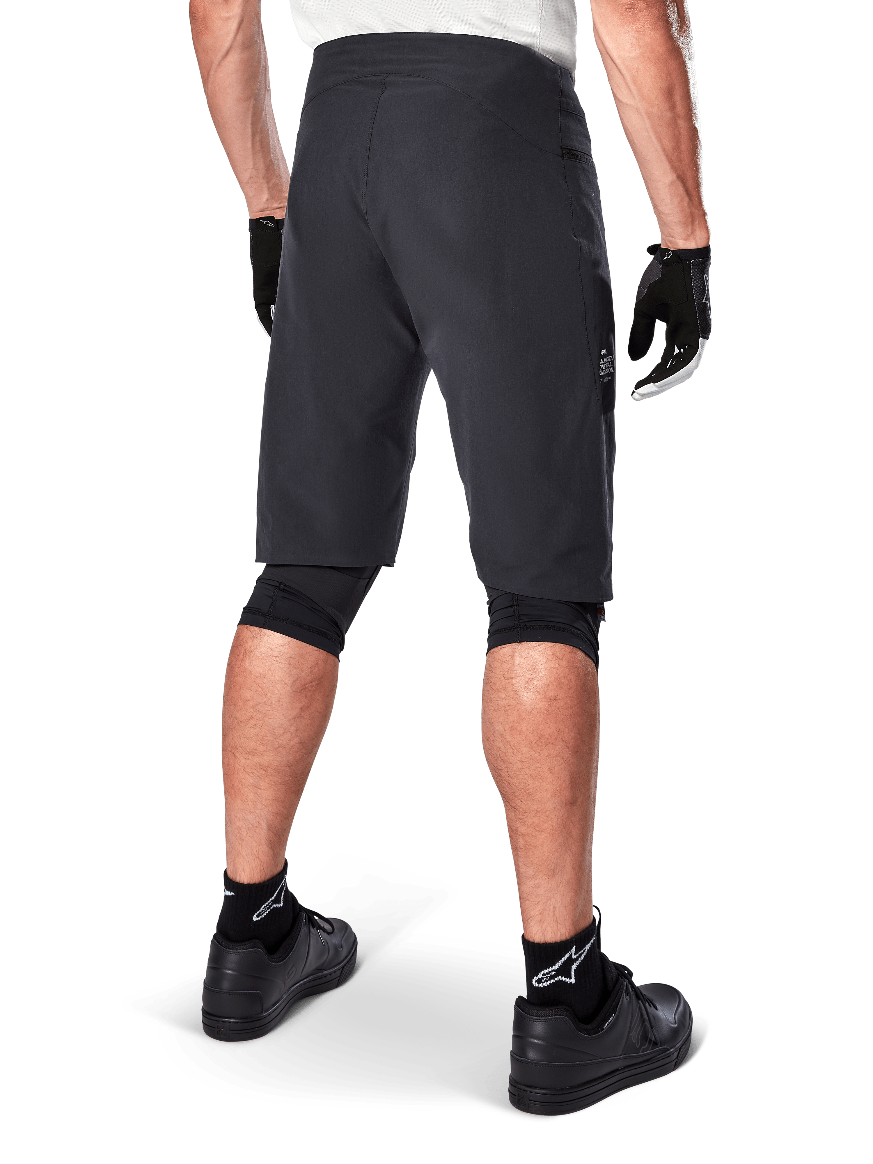 Shorts Alpinestars A-Aria, shorts de ciclismo de montaña, negros, vista trasera que muestra el ajuste de rendimiento y un diseño limpio, usados con guantes negros y calcetines con el logo de Astars en blanco, ropa técnica de ciclismo para conducción off-road