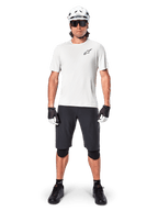 Ciclista de montaña masculino con shorts Alpinestars A-Aria en color negro, combinados con un jersey de rendimiento blanco, casco blanco y rodilleras negras, equipamiento profesional de ciclismo off-road en vista frontal de cuerpo completo