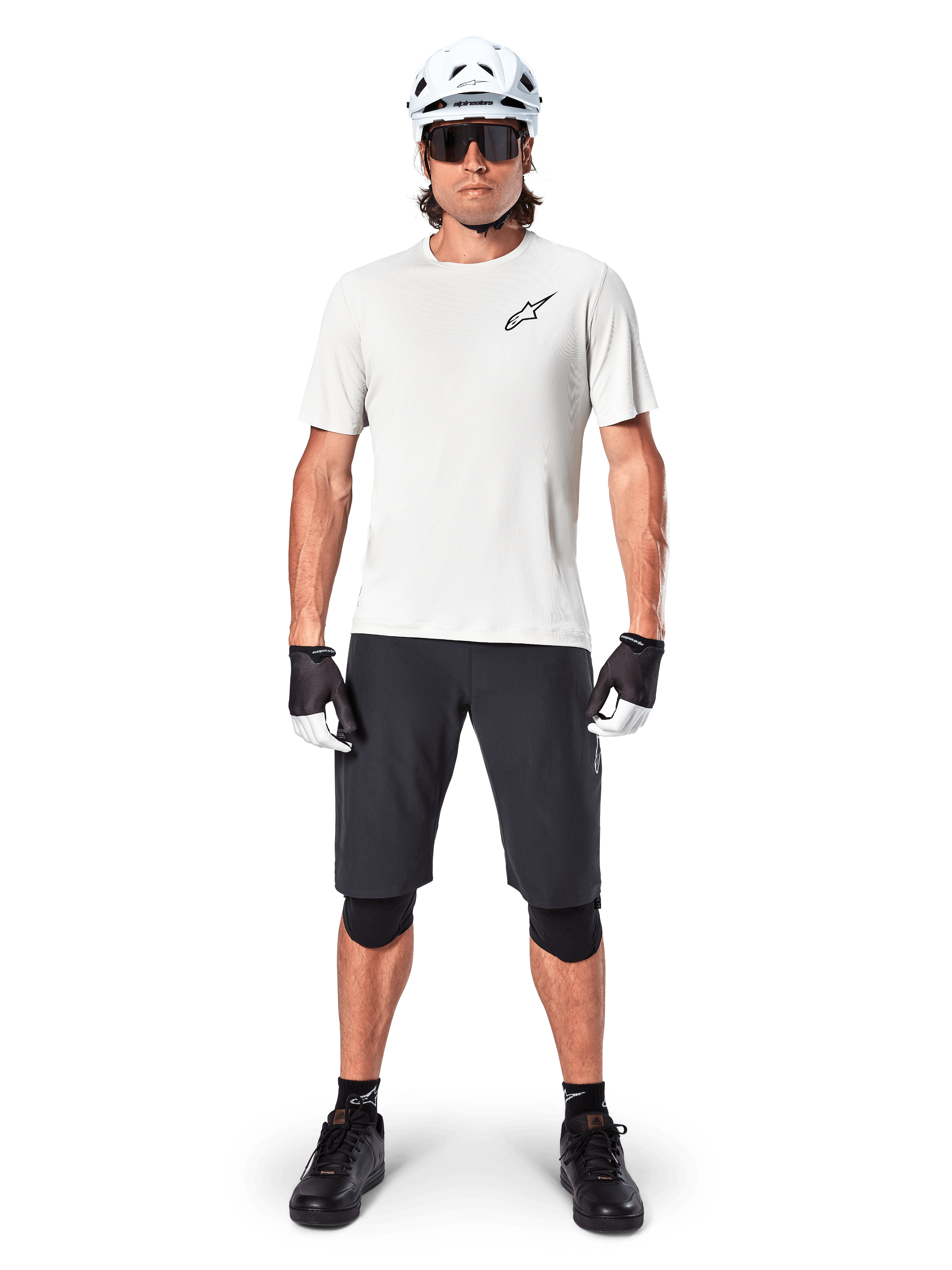 Ciclista de montaña masculino con shorts Alpinestars A-Aria en color negro, combinados con un jersey de rendimiento blanco, casco blanco y rodilleras negras, equipamiento profesional de ciclismo off-road en vista frontal de cuerpo completo