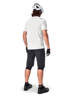 Ciclista de montaña visto desde atrás con shorts Alpinestars A-Aria en color negro, jersey blanco de manga corta de alto rendimiento, casco blanco, guantes negros y zapatillas de ciclismo de montaña negras, equipamiento de ciclismo para trail