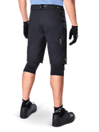 Shorts Alpinestars A-Dura Elite, negros, vista trasera de un ciclista con equipo de bicicleta de montaña que incluye rodilleras negras, guantes y calcetines con logos blancos, con bolsillos laterales con cremallera y detalles reflectantes en un tejido Cordura resistente.