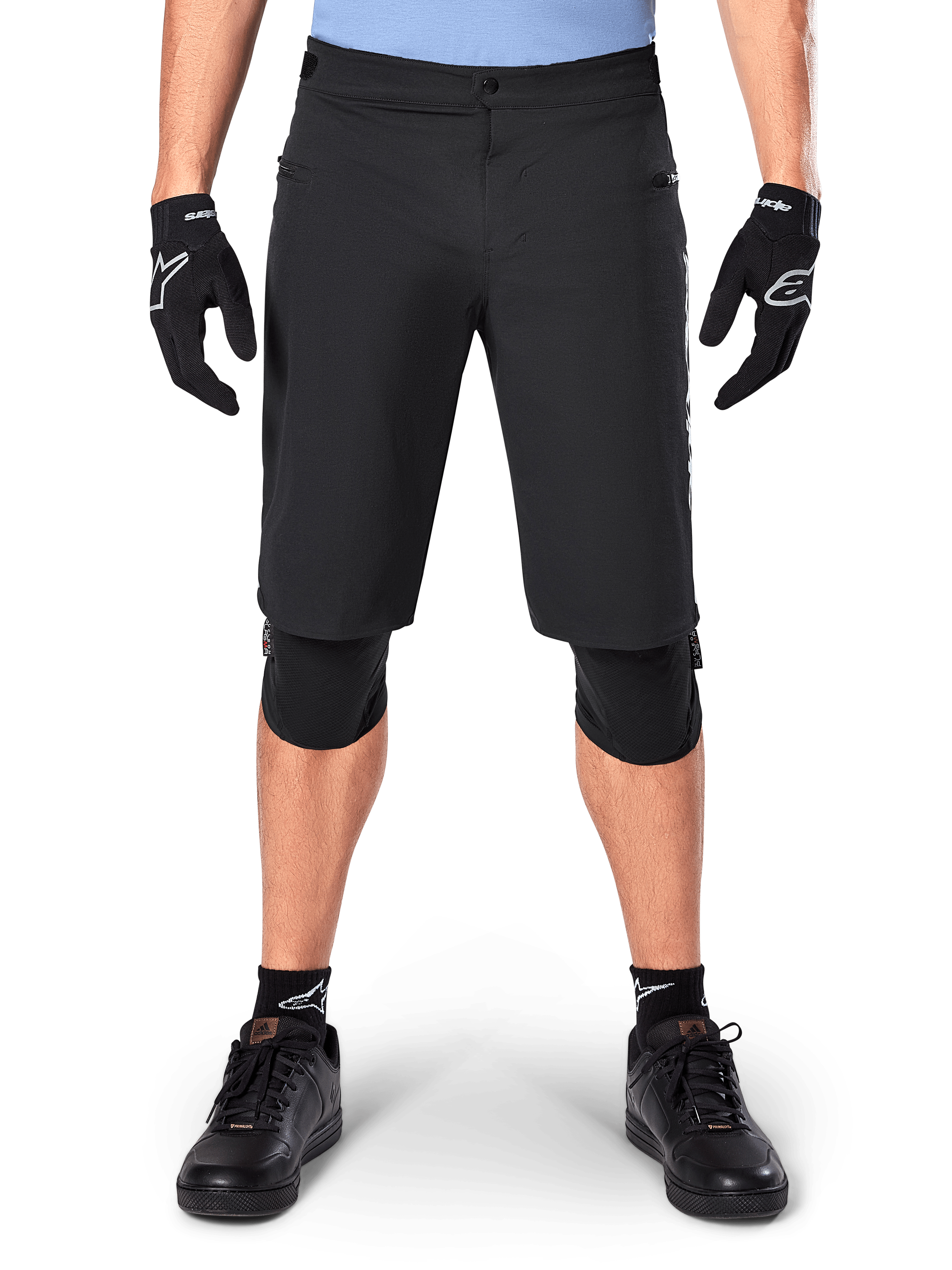 Shorts Alpinestars A-Dura Elite, pantalones cortos negros de mountain bike, usados por un ciclista con guantes negros y rodilleras, con cierre frontal a presión y bolsillos con cremallera, material Cordura duradero para ciclismo de montaña