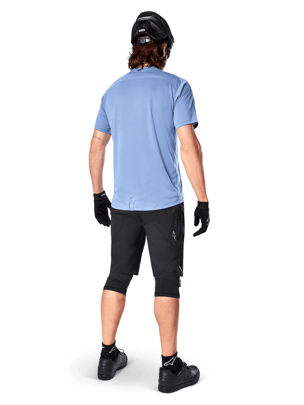Alpinestars A-Dura Elite Shorts, pantalones cortos de ciclismo de montaña, negros, vista trasera en el modelo, usados con camiseta de manga corta azul claro y equipo de protección negro, diseño técnico con bolsillos con cremallera y detalles reflectantes para ciclismo fuera de carretera