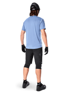 Alpinestars A-Dura Elite Shorts, pantalones cortos de ciclismo de montaña, negros, vista trasera en el modelo, usados con camiseta de manga corta azul claro y equipo de protección negro, diseño técnico con bolsillos con cremallera y detalles reflectantes para ciclismo fuera de carretera