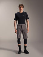 Alpinestars A-Dura Elite Shorts, pantalones cortos de ciclismo de montaña gris oscuro, combinados con una camiseta negra de cuello redondo y rodilleras negras, prenda técnica de longitud hasta la rodilla con cierre frontal a presión y tejido Cordura resistente.