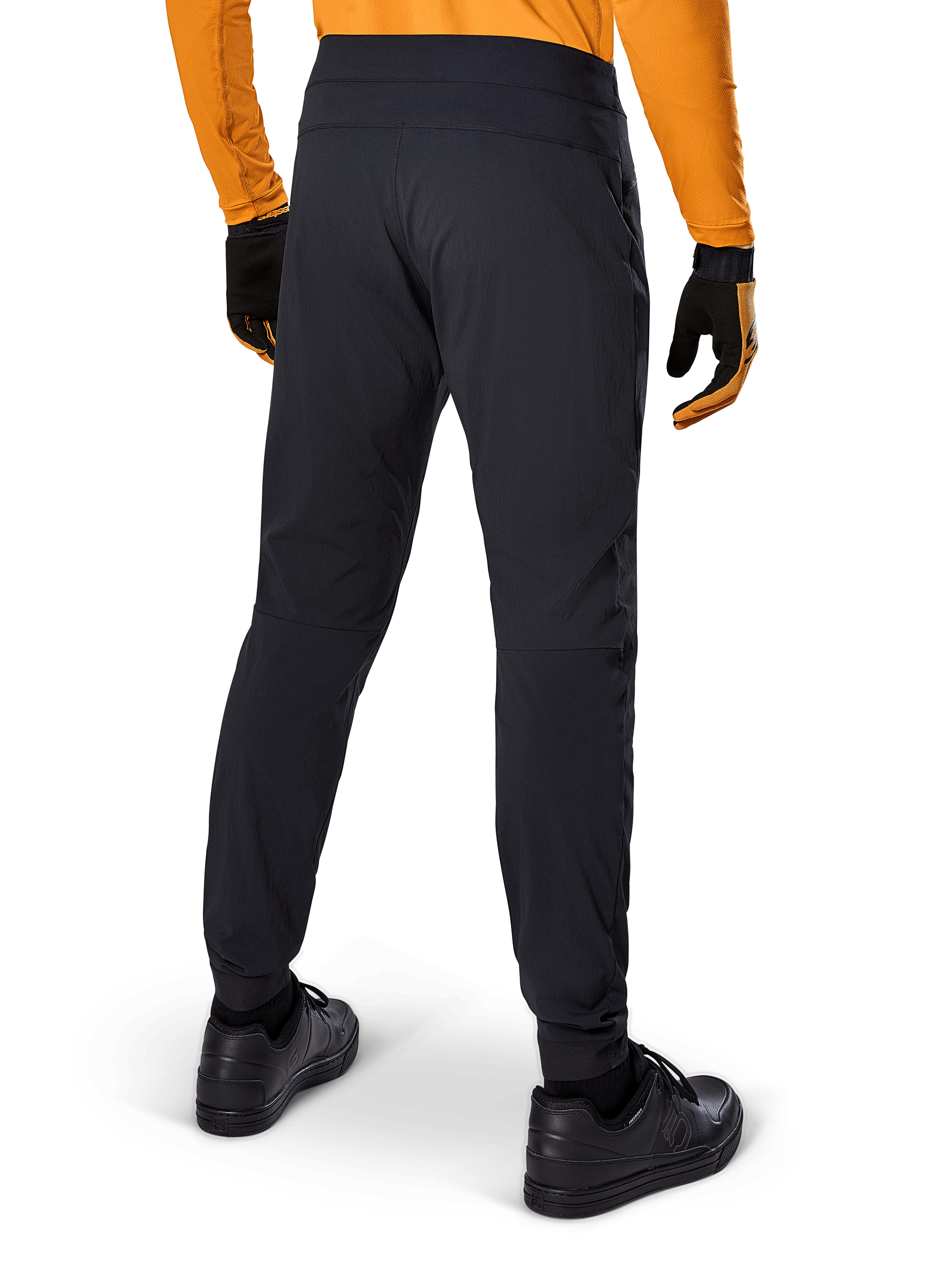 Pantalones Alpinestars A-Dura, pantalones de MTB negros, vista trasera, combinados con un jersey de manga larga naranja y guantes negros, con puños elásticos y material textil duradero para ciclismo de montaña.