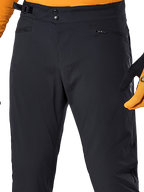 Alpinestars Pantalones A-Dura, pantalones de ciclismo MTB negros, vista de primer plano con cierre de cintura de doble broche, ajustador lateral y bolsillos con cremallera, combinados con un jersey y guantes naranjas