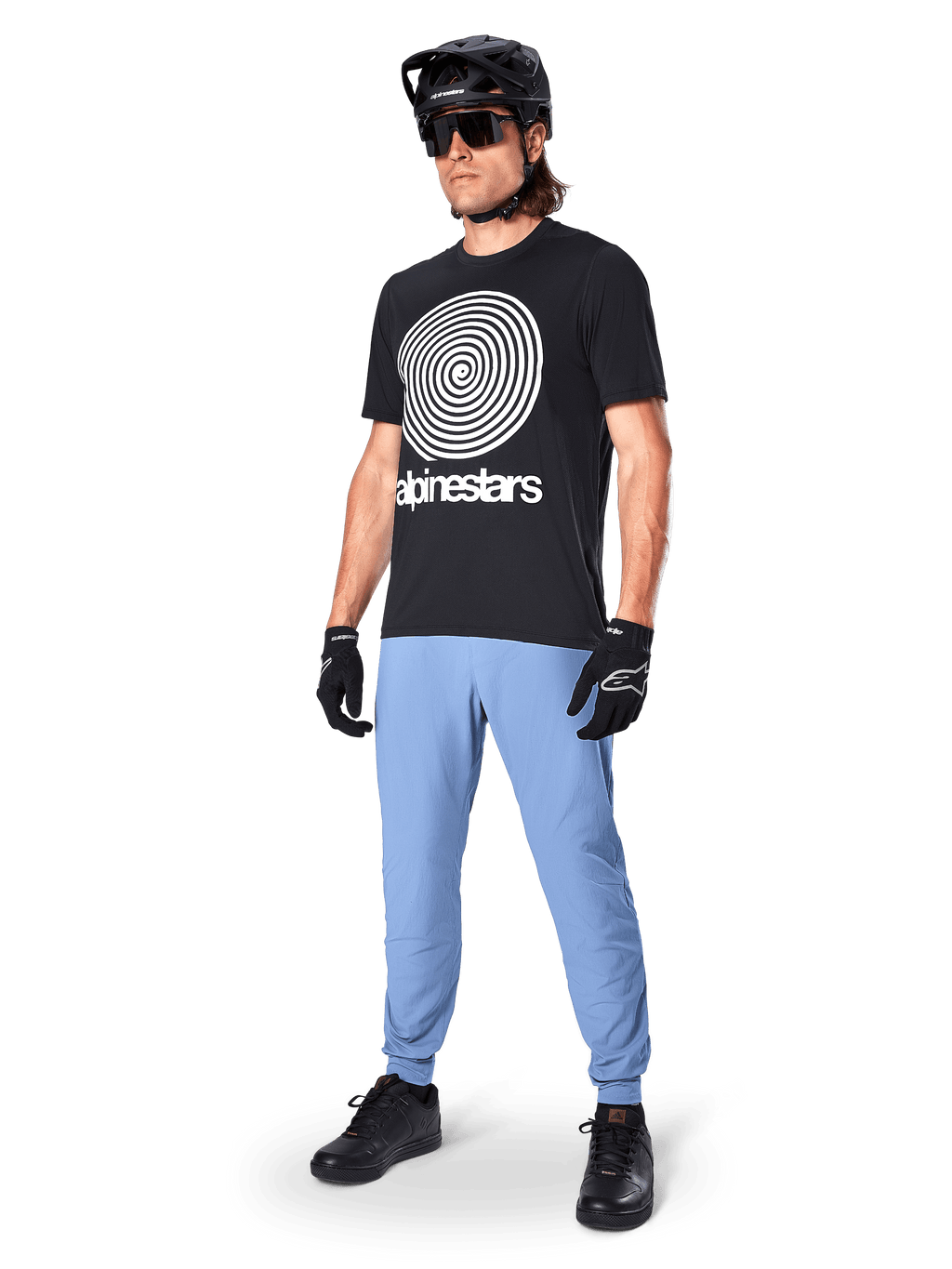 Alpinestars A-Dura Pants, pantalones de MTB, Infinity Blue, usados con una camiseta gráfica negra con un logotipo en espiral blanco, casco negro, gafas de sol y guantes negros, equipamiento profesional de montaña