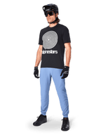 Alpinestars A-Dura Pants, pantalones de MTB, Infinity Blue, usados con una camiseta gráfica negra con un logotipo en espiral blanco, casco negro, gafas de sol y guantes negros, equipamiento profesional de montaña