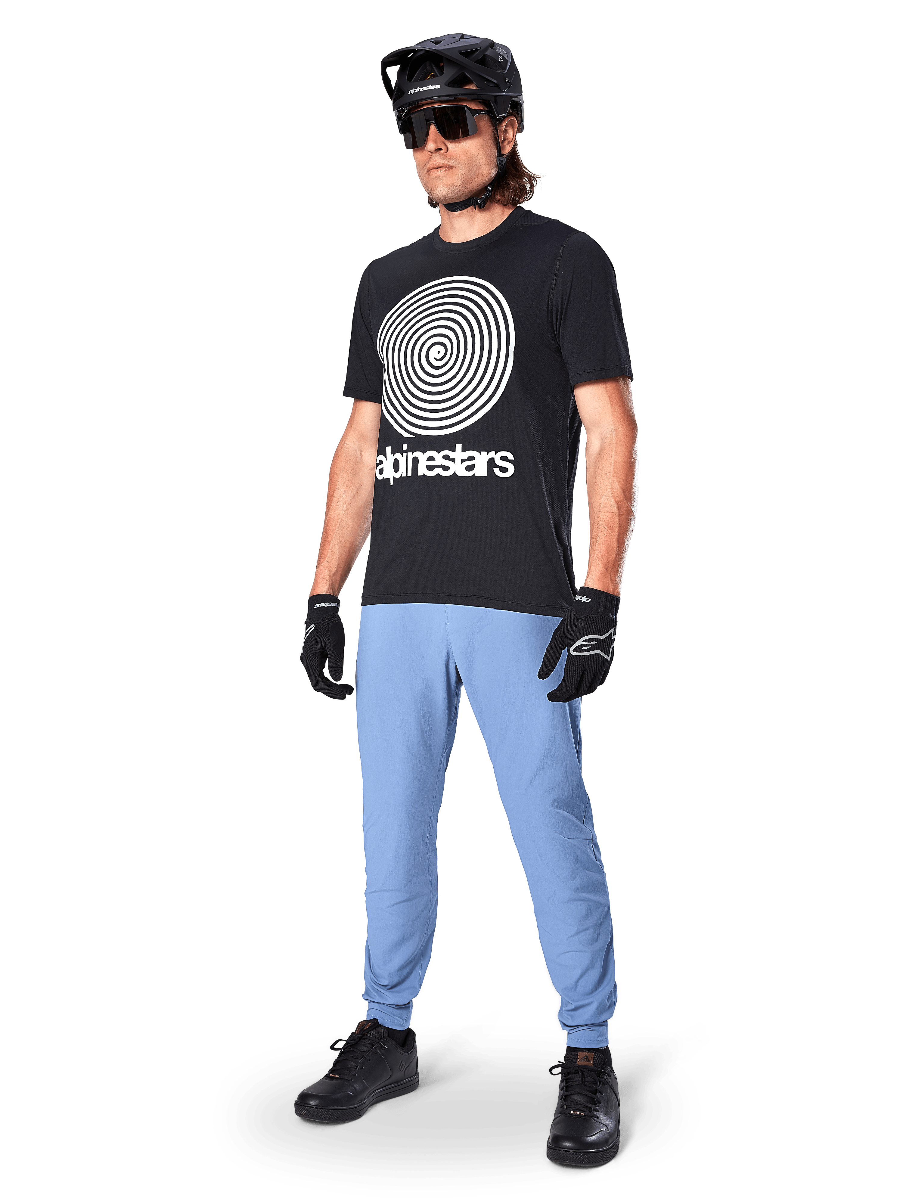 Alpinestars A-Dura Pants, pantalones de MTB, Infinity Blue, usados con una camiseta gráfica negra con un logotipo en espiral blanco, casco negro, gafas de sol y guantes negros, equipamiento profesional de montaña