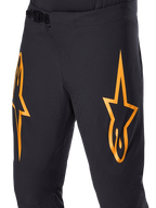 Pantalones Alpinestars A-Supra Race, pantalones de ciclismo MTB negros con grandes logotipos de estrellas naranjas, con cierre de trinquete delantero y orificios de ventilación perforados con láser, diseño técnico de alto rendimiento.