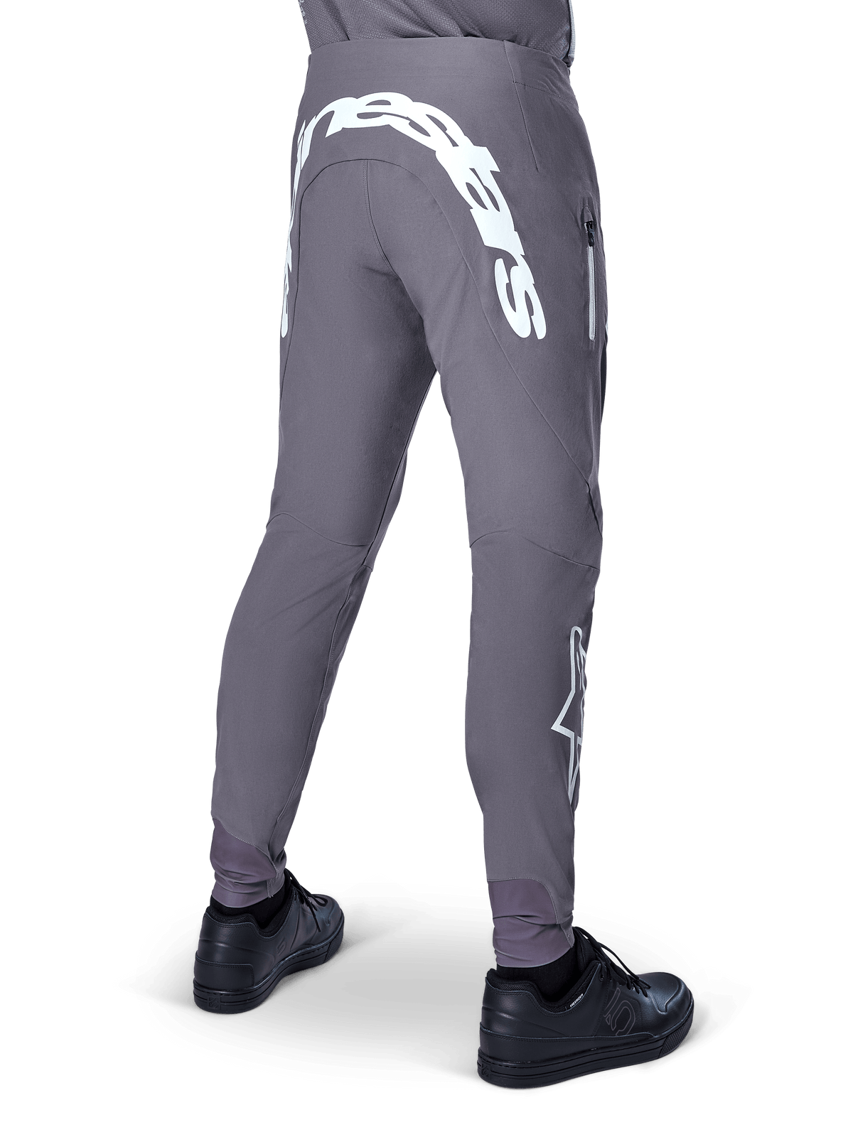 Alpinestars A-Supra Race Pants, pantalones de mountain bike, gris oscuro, vista trasera usados con zapatillas negras, con un gran logotipo blanco de Alpinestars en el canesú trasero y logo de estrella en la pierna, bolsillo con cremallera, tejido elástico de alto rendimiento para MTB
