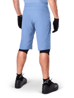 Alpinestars A-Dura Shorts, shorts de mountain bike en color Infinity Blue, vista trasera, combinados con guantes negros, rodilleras y calcetines negros con el logo de la estrella en blanco, material elástico resistente para ciclismo de montaña