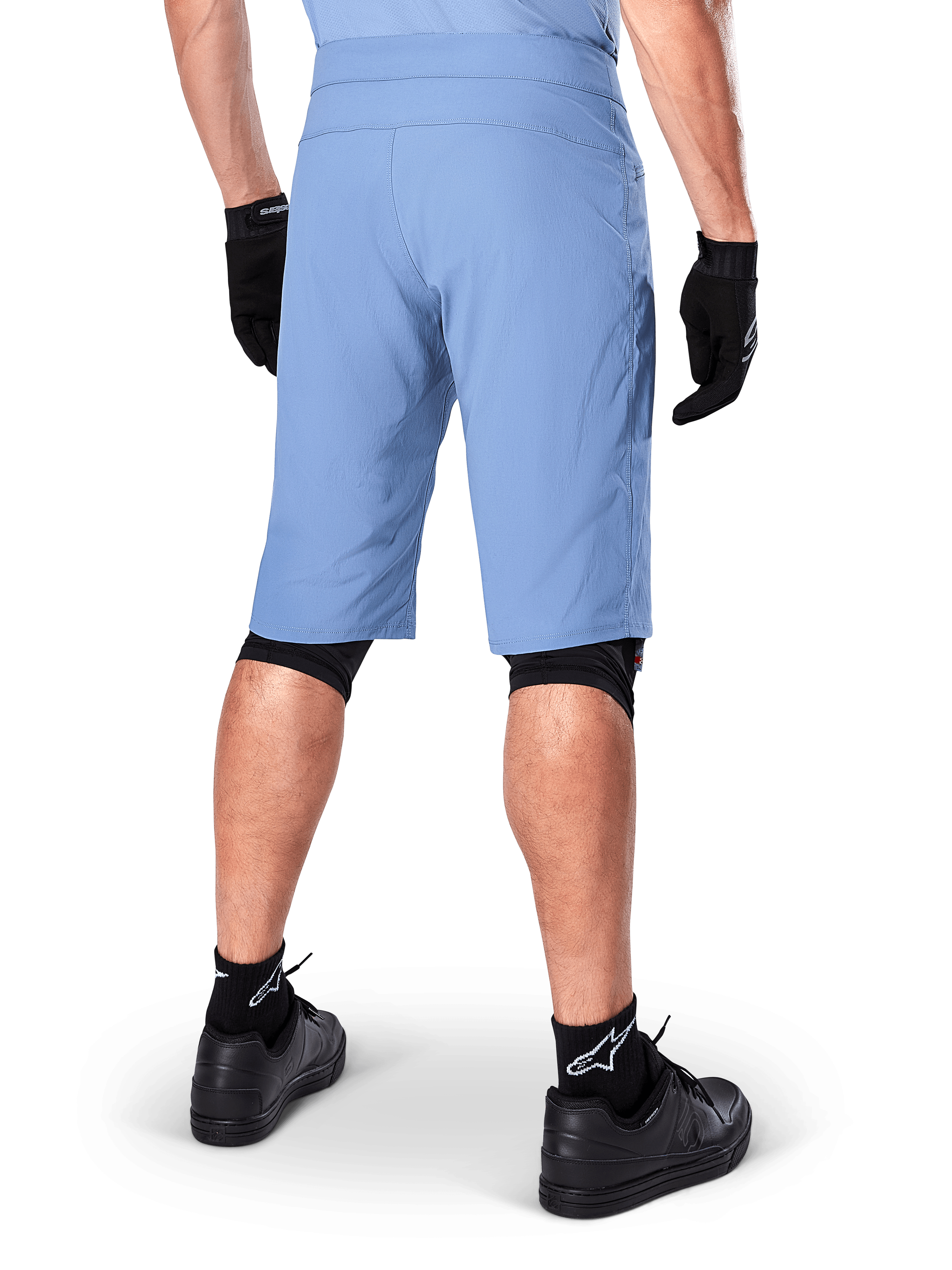 Alpinestars A-Dura Shorts, shorts de mountain bike en color Infinity Blue, vista trasera, combinados con guantes negros, rodilleras y calcetines negros con el logo de la estrella en blanco, material elástico resistente para ciclismo de montaña