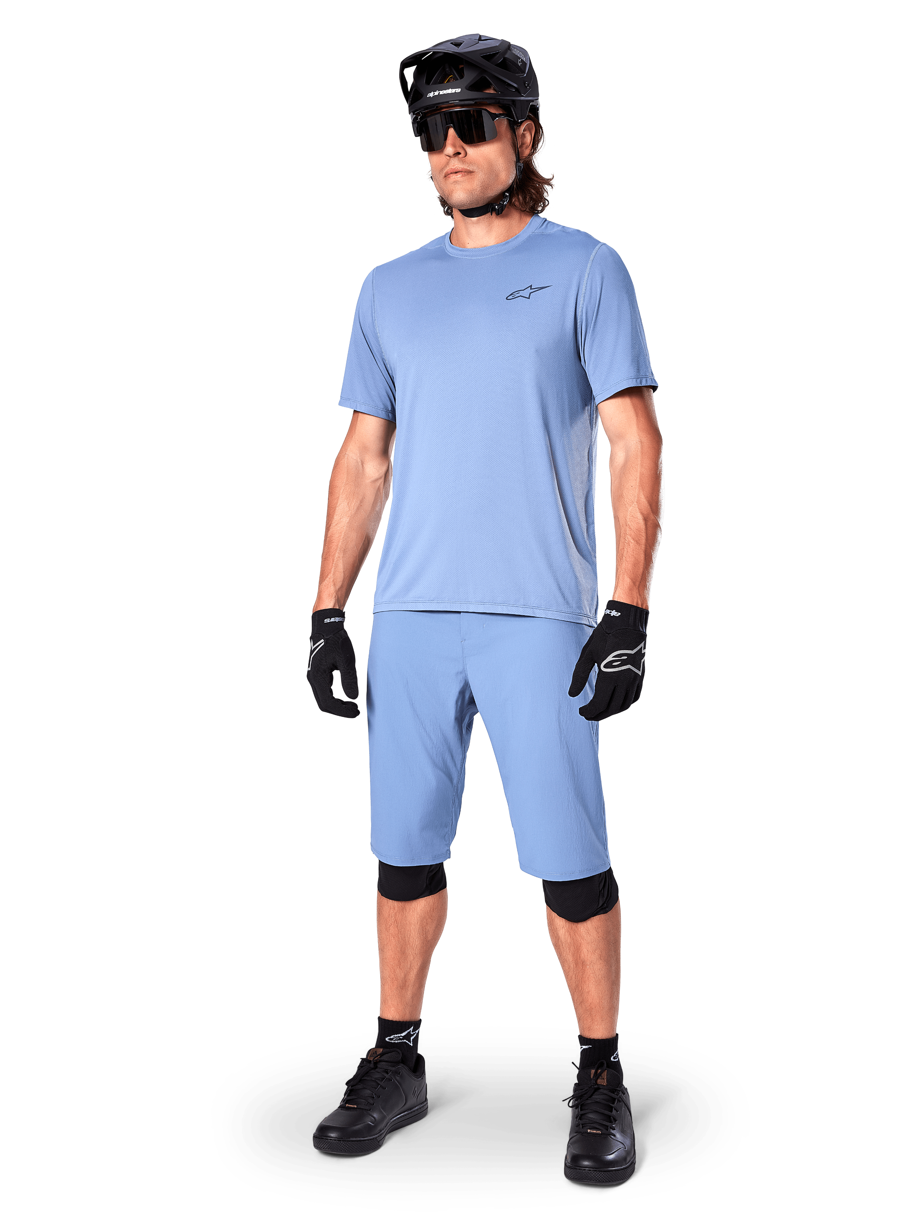 Modelo luciendo los shorts Alpinestars A-Dura en Infinity Blue, jersey de manga corta azul claro a juego, casco de MTB negro, gafas de sol y guantes negros, conjunto completo de ciclismo de montaña para trail