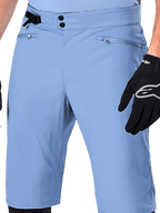 Alpinestars A-Dura Shorts, shorts de ciclismo de montaña en color Infinity Blue, primer plano de la cintura con cierre de doble broche, ajuste lateral ajustable y bolsillos con cremallera y forro de malla, usados con un guante Alpinestars negro