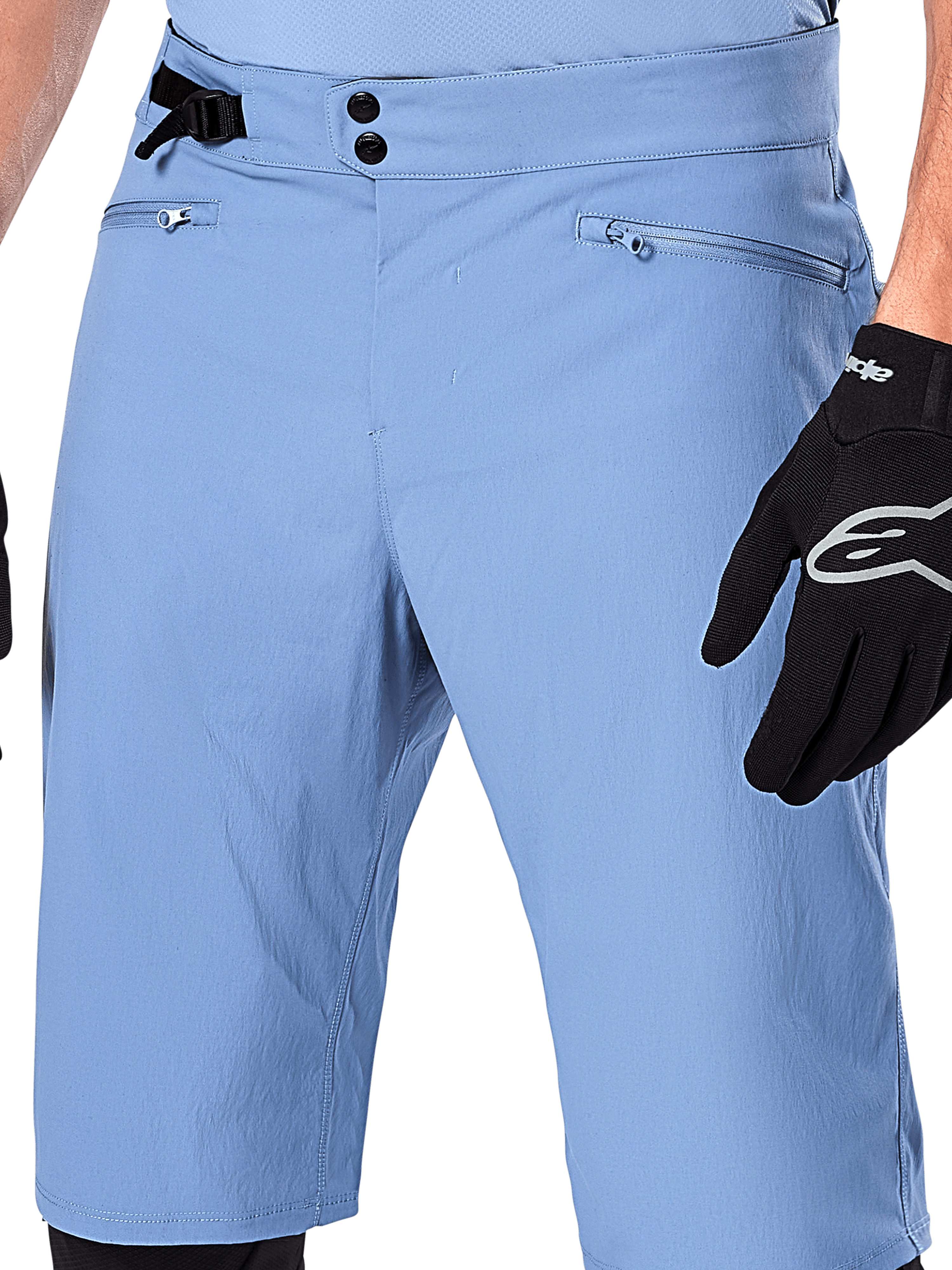 Alpinestars A-Dura Shorts, shorts de ciclismo de montaña en color Infinity Blue, primer plano de la cintura con cierre de doble broche, ajuste lateral ajustable y bolsillos con cremallera y forro de malla, usados con un guante Alpinestars negro