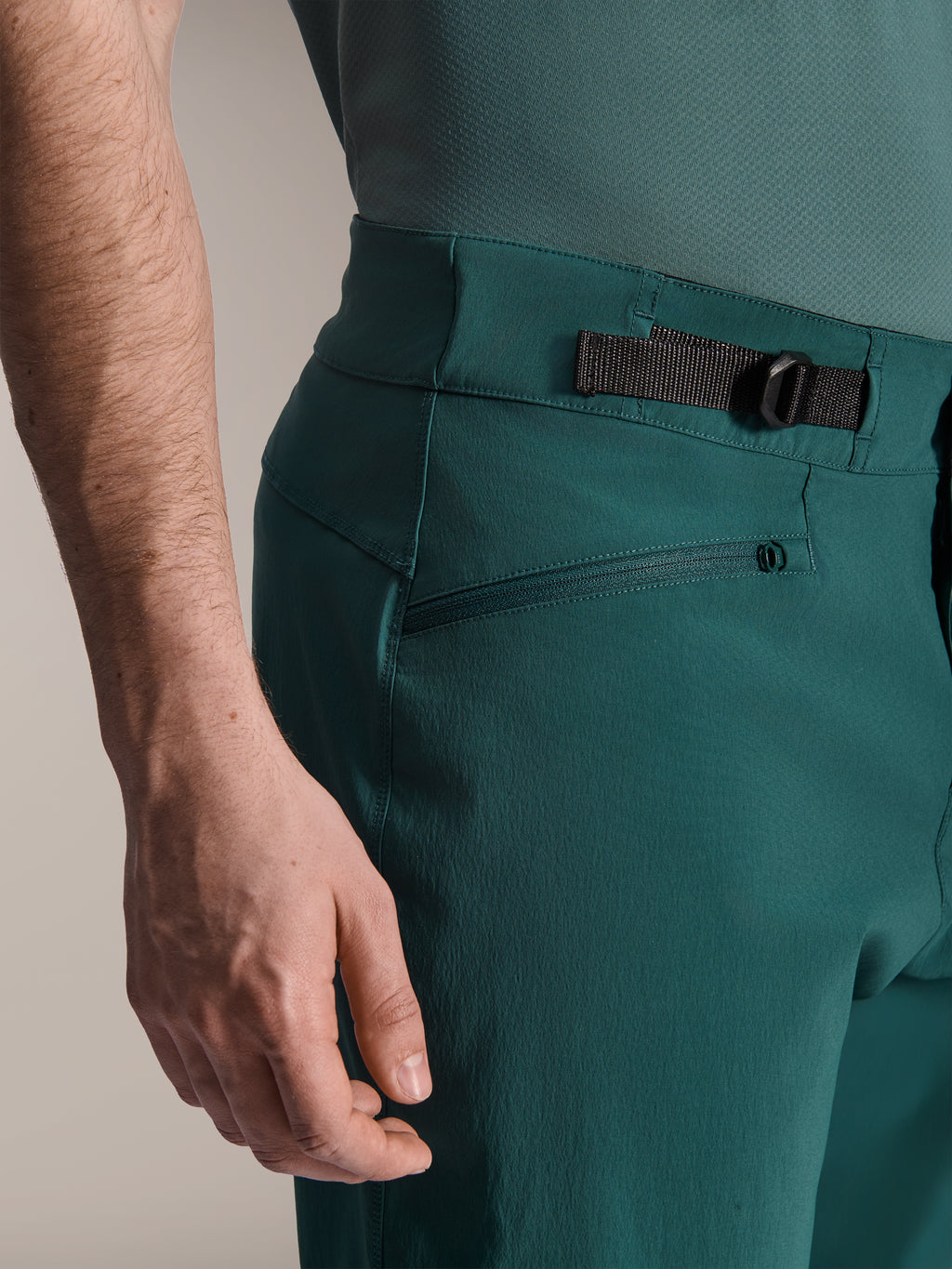 Alpinestars A-Dura Shorts, verde Dark Pine, primer plano del ajustador lateral de cintura y del bolsillo con cremallera, equipamiento duradero de alto rendimiento para ciclismo de montaña.