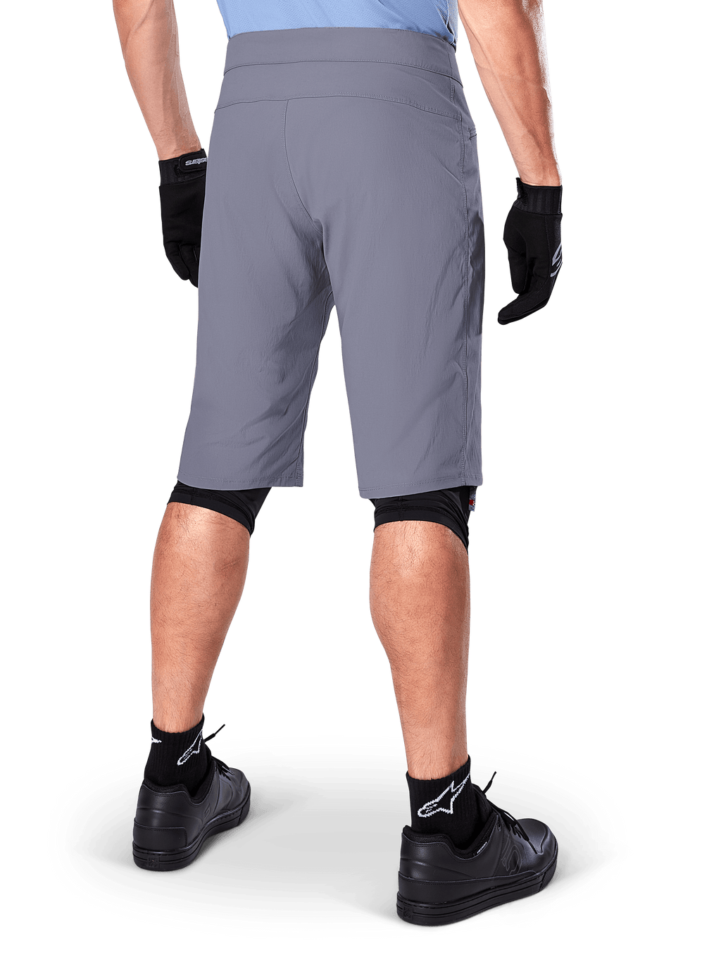 Shorts Alpinestars A-Dura, shorts de mountain bike en color gris oscuro, vista trasera mostrada en un ciclista, usados con guantes negros, mallas para rodillas negras y calcetines negros con el logo de Alpinestars, construcción duradera para ciclismo de montaña